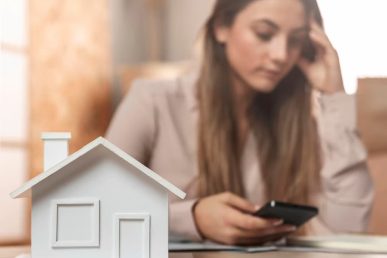 Casa en primer plano con mujer preocupada al fondo